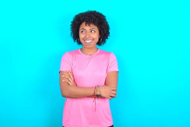 Rüya gibi bir istirahat pembe tişört giyen, mavi arka planda kollarını kavuşturan Afro-Amerikan bir kadın.