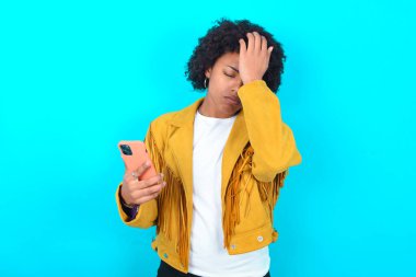 Morali bozuk, mavi arka planda sarı püsküllü ceket giyen genç Afrikalı Amerikalı kadın, cep telefonunun taşıdığı önemli bir şeyi unuttuğu için yüzünü buruşturuyor. Üzüntü ve pişmanlık ifade ediyor.