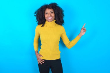 Mavi arka planda sarı boğazlı kazak giyen Afro-Amerikalı bir kadın parmak boşluğu satışlarını gösteren kameraya bakıyor.