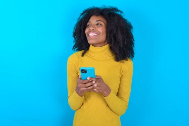 Mavi arka planda sarı boğazlı kazak giyen Afro-Amerikalı kadın elinde akıllı bir telefonla boş bir telif alanına bakıyor..
