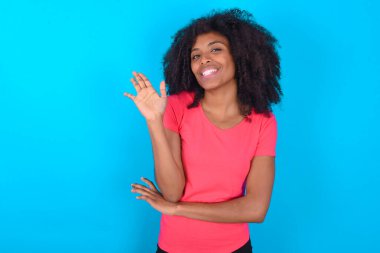 Mavi arka plan üzerine pembe tişört giyen başarılı Afro-Amerikan kadın avucunu kaldırıyor ve arkadaşları tarafından eğlendirilmekten zevk alarak gözlerini kapıyor.