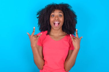 Mavi arka planda pembe tişört giyen Afro-Amerikalı kadın rock 'n roll tabelasını kendinden emin ve neşeli gösteriyor. Partide havalı müzikten hoşlanıyor. Vücut dili kavramı.