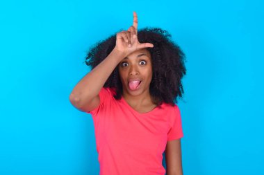 Mavi arka plan jestleri üzerine pembe tişört giyen Afro-Amerikalı bir kadın. Alnında parmak olan bir jest insanların dil göstermesiyle dalga geçiyor.