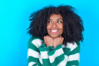 Mavi arka planda çizgili süveter giyen Afro-Amerikalı kadın çene altında el ele tutuşuyor.