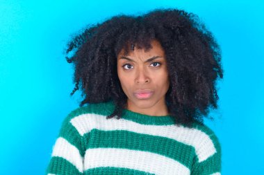 Mavi arka planda çizgili süveter giyen Afro-Amerikalı bir kadın. İlan veren parmaklarıyla işaret ediyor, şaşırmış yüzünü ve ağzını açıyor.