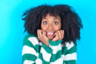 Mavi arka planda çizgili süveter giyen Afro-Amerikalı kadın boş bir uzay evi gibi görünüyor.