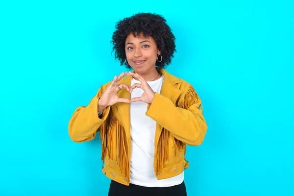 Poważna Młoda Afroamerykanka Żółtej Kurtce Niebieskim Tle Trzyma Ręce Skrzyżowane — Zdjęcie stockowe