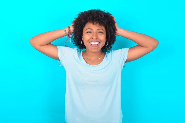 Radosna Afroamerykanka Afro Fryzurą Niebieskiej Koszulce Niebieskim Tle Reaguje Podnosząc — Zdjęcie stockowe