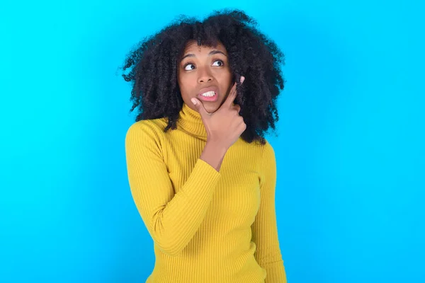 Afro Amerikaanse Vrouw Draagt Gele Coltrui Blauwe Achtergrond Denkend Bezorgd — Stockfoto