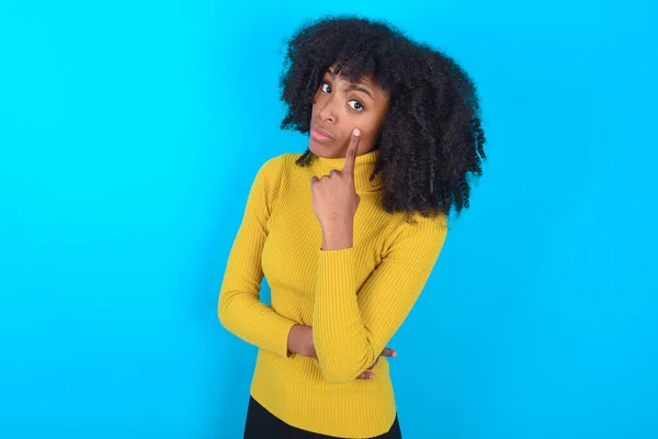 Afroameričanka Žlutém Roláku Modrém Pozadí Ukazuje Oko Dívá Jak Gestikuluješ — Stock fotografie