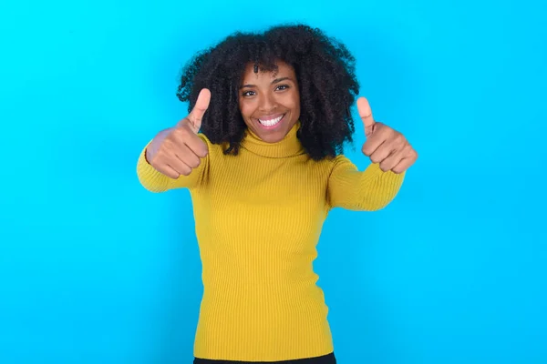 Afroamerykanka Żółtym Golfie Niebieskim Tle Aprobująca Pozytywny Gest Ręką Uśmiechem — Zdjęcie stockowe