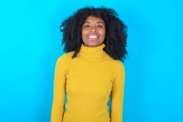 顔に幸せとクールな笑顔で青の背景に黄色のタートルネックを身に着けているアフリカ系アメリカ人女性 運のいい人 — ストック写真
