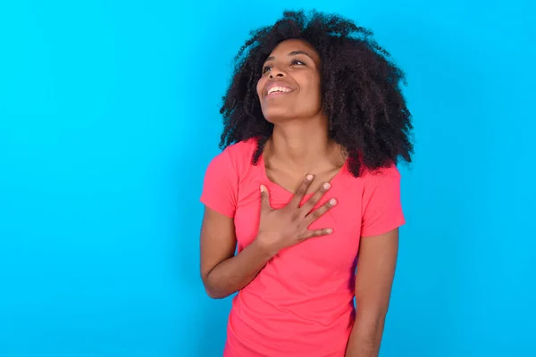 青い背景にピンクのTシャツを着た楽しいアフリカ系アメリカ人女性は ポジティブな感情を表現しています — ストック写真