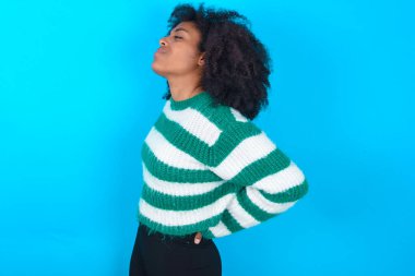 Mavi arka planda çizgili süveter giyen Afro-Amerikalı kadın sırt ağrısı çekti.