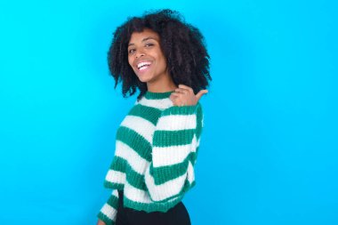 Mavi arka planda çizgili süveter giyen etkileyici Afrikalı Amerikalı kadın.