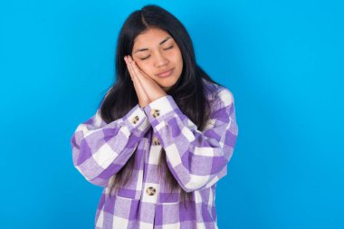 Mavi arka planda ekose gömlekli genç Latin kadın uyuyordu. Yorgun düşler görüyordu ve elleri ile poz veriyordu. Gözleri kapalıydı..