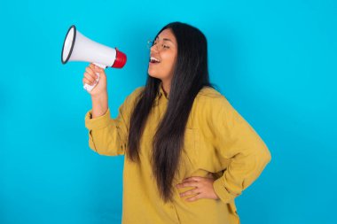 Mavi arka plan üzerine sarı tişört giyen komik Latin kadın. İnsanlar samimi duygular ve yaşam tarzı kavramı. Kopyalama alanı oluşturun. Megafonla bağırıyordu..