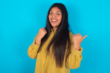 Yaşasın havalı genç Latin kadın mavi arka plan üzerinde sarı gömlek giyen boş uzay eli yumruğu.