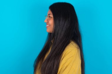 Mavi arka planda sarı gömlekli hoş Latin bir kadının profil portresi boş dişli bir gülümsemeye benziyor.