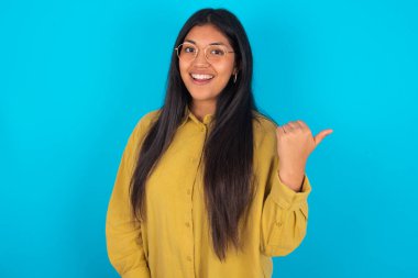 Mavi arka plan üzerinde sarı tişört giyen etkileyici genç Latin kadın.