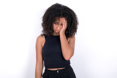 Tired overworked Young African American woman wearing black T-shirt over white background has sleepy expression, gloomy look, covers face with hand, has eyes shut, gasps from tiredness, fatigue after party