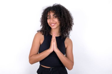 Young African American woman wearing black T-shirt over white background praying with hands together asking for forgiveness smiling confident.