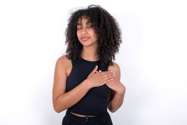 Young African American woman wearing black T-shirt over white background smiling with hands on chest with closed eyes and grateful gesture on face. Health concept.