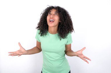 Young African American woman wearing green T-shirt over white background crazy and mad shouting and yelling with aggressive expression and arms raised. Frustration concept.