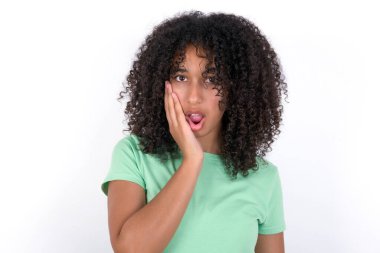 Shocked Young African American woman wearing green T-shirt over white background looks with great surprisment being very stunned, astonished with unexpected news, Facial expressions concept.
