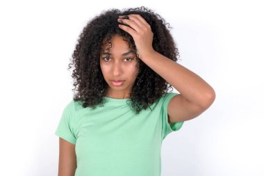 Embarrassed Young African American woman wearing green T-shirt over white background with shocked expression, expresses great amazement, Puzzled model poses indoor
