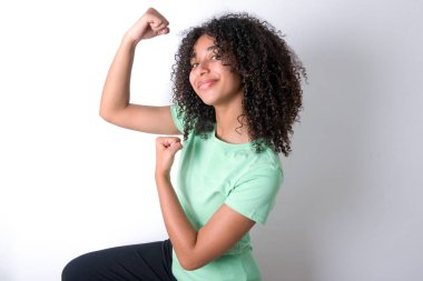 Profile photo of excited Young African American woman wearing green T-shirt over white background raising fists celebrating black Friday shopping