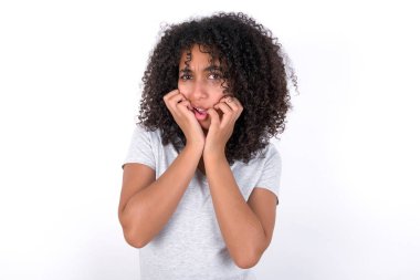 Speechless Young African American woman wearing grey T-shirt over white background keeps hands near opened mouth reacts to shocking news stares wondered at camera