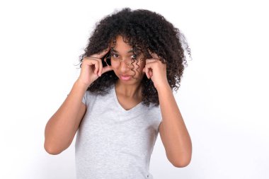 Serious concentrated Young African American woman wearing grey T-shirt over white background keeps fingers on temples, tries to ease tension, gather with thoughts and remember important information for exam