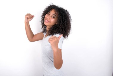 Hooray cool Young African American woman wearing grey T-shirt over white background point back empty space hand fist