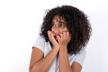 Terrified Young African American woman wearing grey T-shirt over white background looks empty space home alone moonless night