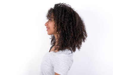 Profile portrait of nice Young African American woman wearing grey T-shirt over white background look empty space toothy smile