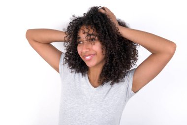 Cheerful overjoyed Young African American woman wearing grey T-shirt over white background reacts rising hands over head after receiving great news.