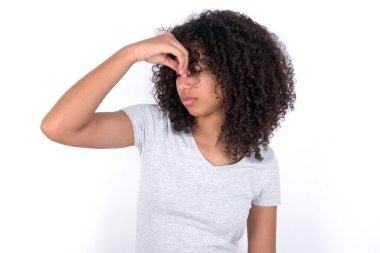 Sad Young African American woman wearing grey T-shirt over white background suffering from headache holding hand on her face