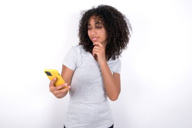 Thoughtful happy Young African American woman wearing grey T-shirt over white background hold look phone, copyspace