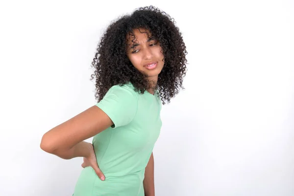 若いアフリカ系アメリカ人女性が白い背景に緑色のTシャツを着て腰痛に苦しみ 手で触れ 筋肉痛 — ストック写真