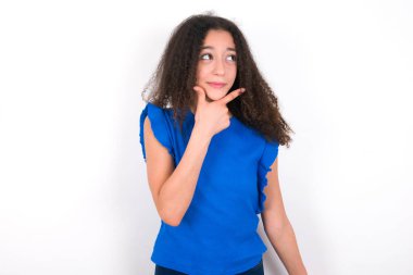 Beyaz arka plan üzerinde mavi tişört giyen afro saçlı genç kız bir soru hakkında endişeli ve gergin bir şekilde düşünüyor..