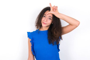 Afro saçlı genç kız beyaz arka planda mavi tişört giyiyor. Alnında parmakları olan insanlarla dalga geçiyor. Ezik jestler yapıyor, alay ediyor ve hakaret ediyor..