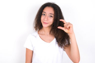 Beyaz arka plan üzerine beyaz tişört giyen hoşnutsuz genç kız küçük el işaretleri çok büyük olmayan bir şeyi gösteriyor. Vücut dili kavramı.