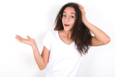 Şaşırmış afro saçlı beyaz tişörtlü genç kız beyaz arka planda el ele tutuşup teklif sunuyor.