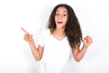 Beyaz arka plan noktalarının üzerine beyaz tişört giyen afro saçlı genç kız yumruğunu kaldırıp, birinci sınıf jest yapıyor..