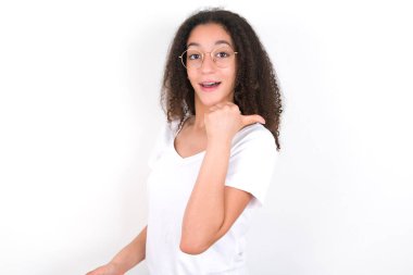 Afro saçlı, beyaz arka plan noktasında beyaz tişört giyen etkileyici bir genç kız.