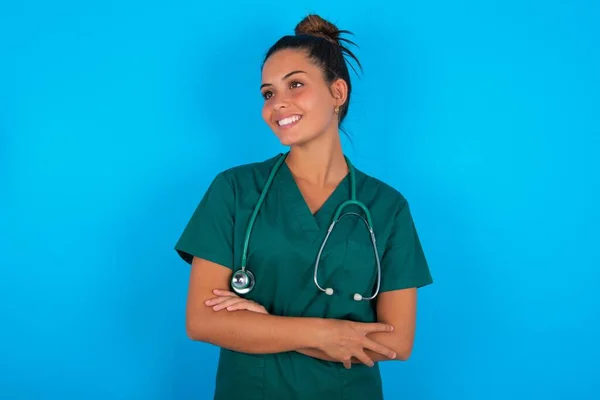 夢のような残りの部分は 青の背景交差腕の上に緑の医療制服を着て美しいヒスパニック系の医師の女性をリラックス 良いコピースペースに見えます — ストック写真