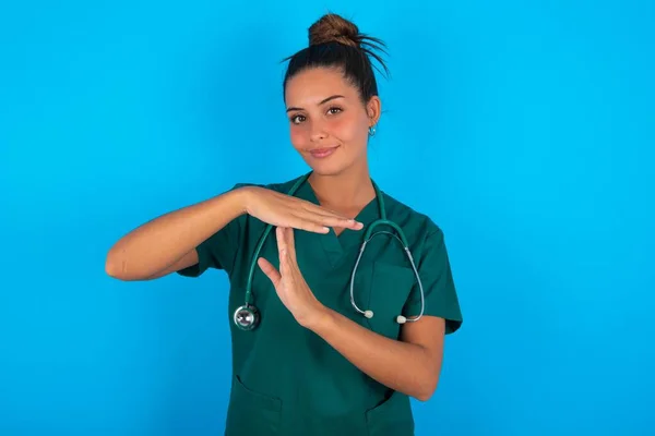 青い背景の上に緑色の制服を着た美しいヒスパニック系の医師の女性は タイムアウトジェスチャーを示す動揺しています 停止する必要があります ハードワーク後に休息のための時間を尋ねます — ストック写真