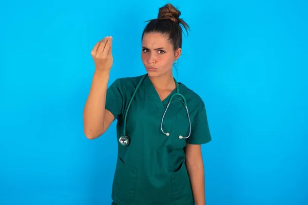 青い背景に緑色の制服を着た美しいヒスパニック系の医師の女性怒りのジェスチャー手で典型的なイタリアのジェスチャー カメラを探して — ストック写真