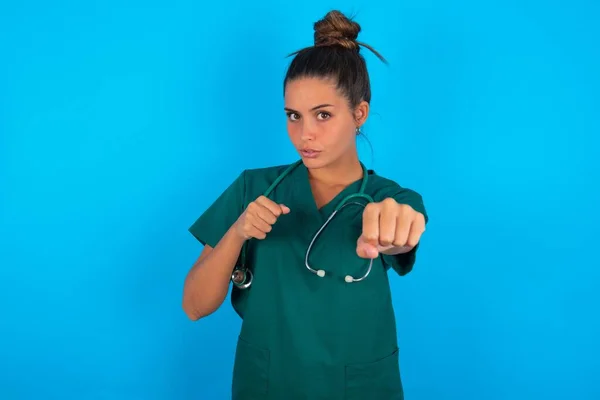 青い背景に緑の制服を着た美しいヒスパニック系の医師の女性戦うために拳をパンチ 積極的かつ怒りの攻撃 脅威と暴力 — ストック写真